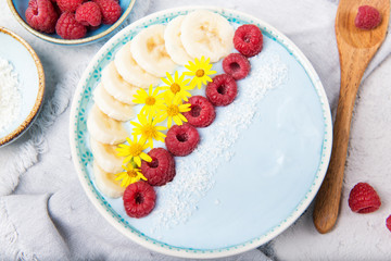 Blue yogurt smoothie bowl made with blue spirulina powder, fresh berries, banana and yellow flowers, top view