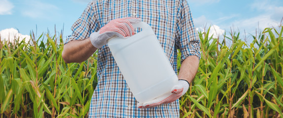 Farmer holding pesticide chemical jug in cornfield - obrazy, fototapety, plakaty