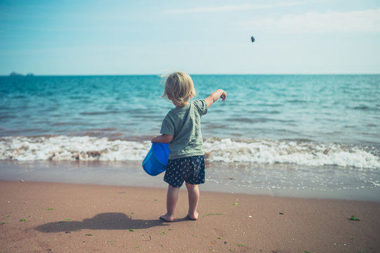 Toddler on the beach throwing stones in the sea