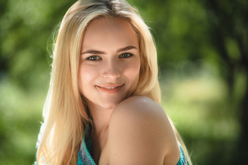 Sweet young lady outside in forest. Portrait of lovely looking girl wearing off shoulder turqouise sweater smiling taken outdoors in park.