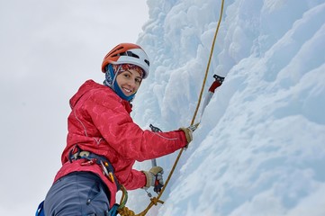 Alpinist woman with  ice tools axe in orange helmet climbing a l