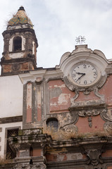 Ancient italian church with small cross and old clock. Time and religion concept. Historical ruins. Religion and timeless concept. Vintage exterior building. Abandoned church. Outdoor clock. 