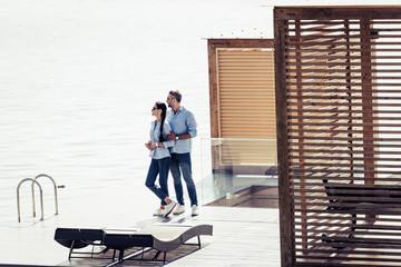 stylish couple standing on pier near lake at country house