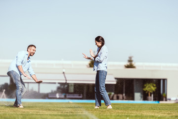 Obraz premium couple having fun with automatic watering on green lawn near country house