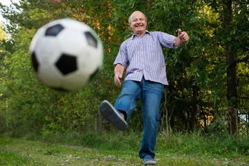 Foto op Canvas Old man in seventies kicking a soccer ball on playground © RealPeopleStudio