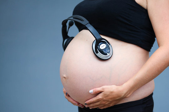 Pregnant woman's belly. Unborn child listens to music with headphones.