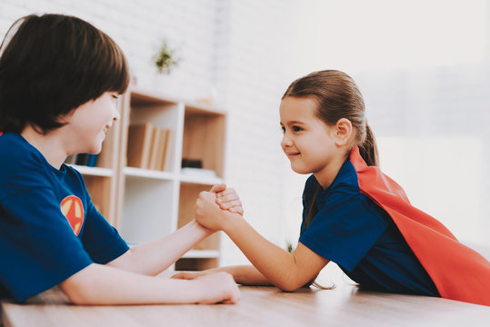 Girl And Boy Arm Wrestling In Superhero Suits.