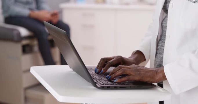 Close view of laptop computer and medical doctor typing notes. Close-up of senior black doctor typing on portable notebook computer insude clinic