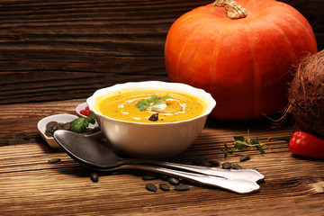 Roasted pumpkin and carrot soup with cream and pumpkin seeds on wooden background.