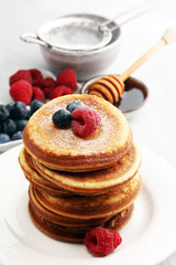Pancakes with berries and maple syrup on rustic table