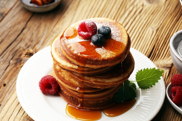 Pancakes with berries and maple syrup on rustic table