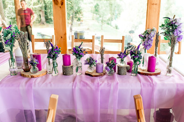 Purple lavender wedding. Table decor with dry lavender, green and white flowers. Candles, wooden rustic vases, Glass jars, lace bottles, sawed wood.