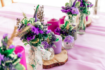 Obraz na płótnie Canvas Purple lavender wedding. Table decor with dry lavender, green and white flowers. Candles, wooden rustic vases, Glass jars, lace bottles, sawed wood.