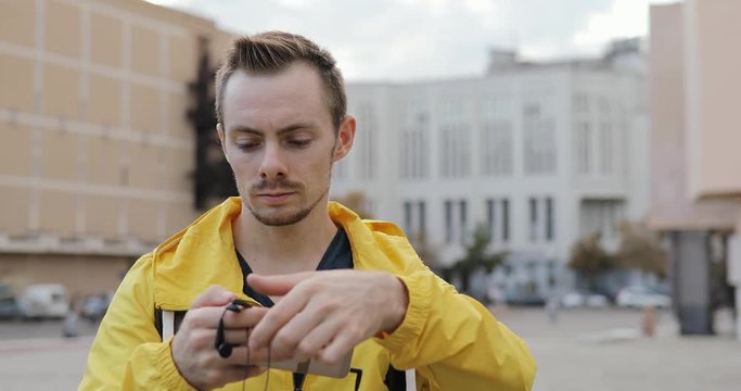 Portrait of young caucasian man puts on earphones in urban city square