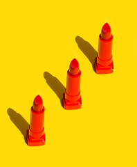 Three red crimson lipsticks arranged in diagonal on solid yellow background. Bright sunlight strong shadows. Creative minimalist funky style pop art. Poster banner design element copy space