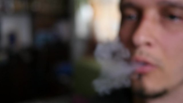Man smoking Electronic Cigarette at home closeup breathing out a smoke