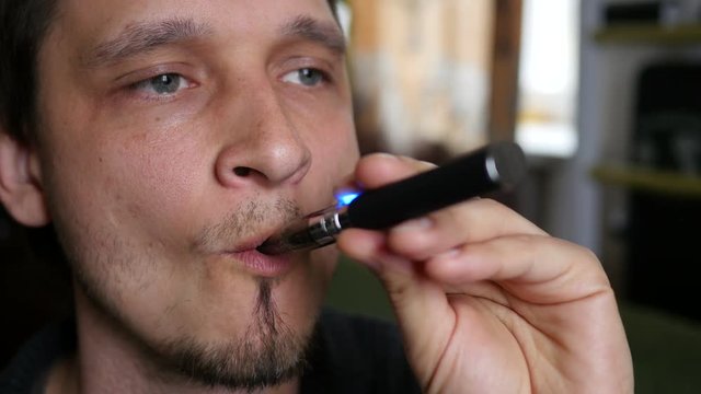 Man smokes electronic cigarette at home exhaling smoke face closeup
