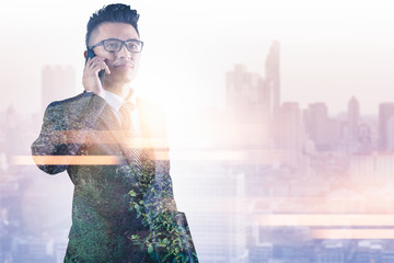 The double exposure image of the businessman using a smartphone during sunrise overlay with nature image. The concept of telecommunication, technology, 5g and internet of things.