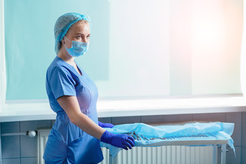 Young blond woman assistant standing near table with equipment prepating for gynecology operation....