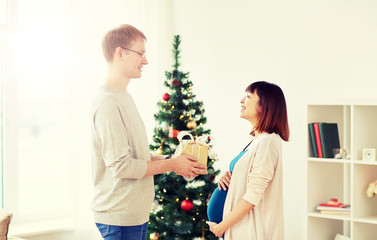 pregnancy, winter holidays and people concept - happy husband giving christmas present to his pregnant wife at home