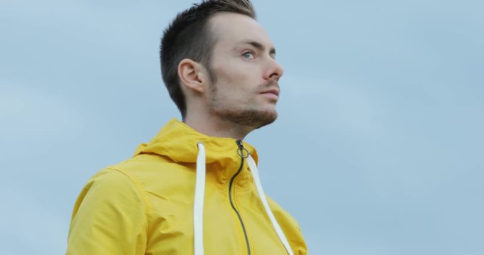 Man in fashionable yellow jacket looking around cloudy sky wearing hood