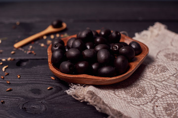 Black olives in the bowl on wood background with spoon