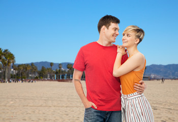 travel, tourism and summer holidays concept - happy smiling couple hugging over venice beach background in california