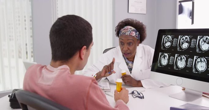 Middle aged black doctor showing young patient results of his brains ct-scan. Portrait of male patient receiving anti-inflammatory medication for his head