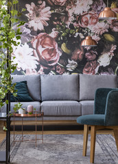 Green chair and copper table on patterned rug in living room interior with grey settee. Real photo