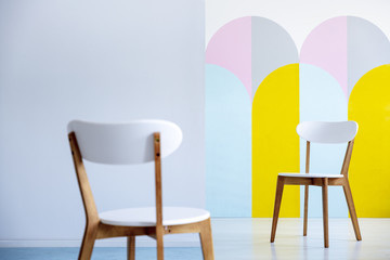 Two white chairs facing each other in a bright office interior with pastel decorations. Real photo...