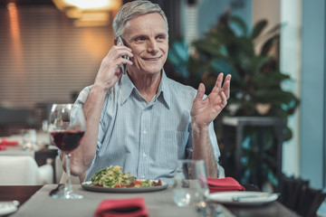 I am here. Positive mature man keeping smile on face while having pleasant conversation