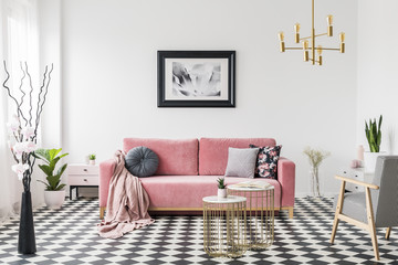Poster above pink sofa in spacious living room interior with patterned armchair and plants. Real...
