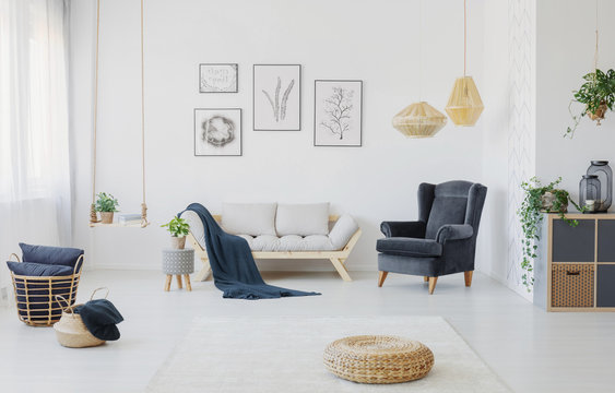 Real photo of a living room interior with a sofa, armchair, posters on a wall and wicker pouf