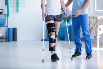 Sport physiotherapist and patient with leg injury during training with crutches - 221994202