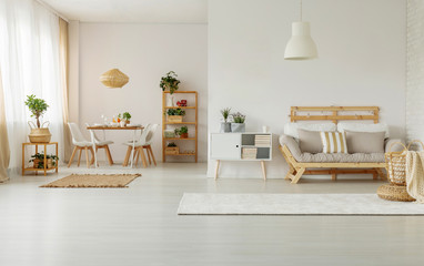 White cabinet with plants next to wooden couch in apartment interior with chairs at table. Real photo