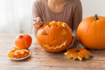 halloween, decoration and holidays concept - close up of woman with spoon carving pumpkin flesh and making or jack-o-lantern at home