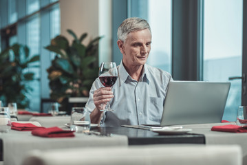 Online conference. Delighted mature man keeping smile on his face while spending day in favorite cafe