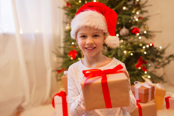 christmas, holidays and childhood concept - smiling girl in santa helper hat with gift box at home