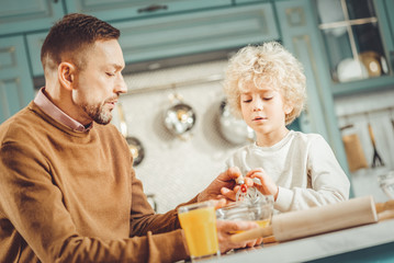 Communicating with son. Bearded dark-haired man feeling memorable communicating with son in spacious kitchen