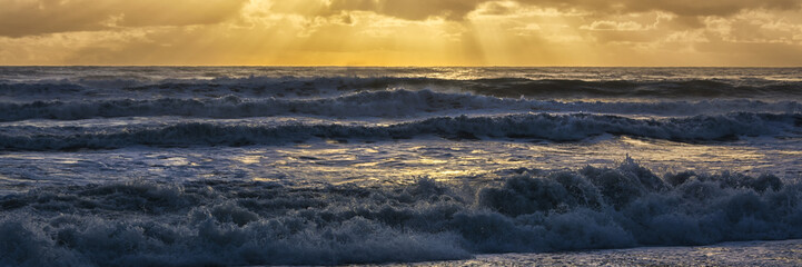 Beautiful sunset panorama view on the westcoast of New Zealand, near Punakaika. The tidal waves are rolling on the beach while the warm orange sun goes down at the end of the day.