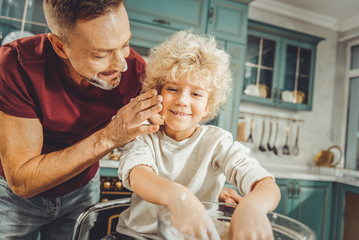 Obraz premium Caring father. Caring dark-haired father looking at his curly blonde-haired son while baking pastry together