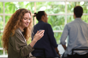 Young businesswoman using smartphone in the office with colleagues in the background