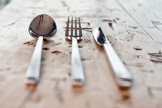 L&ouml;ffel, Gabel und Messer nebeneinander gelegt auf alten gravierten Tisch