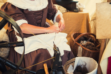 Cropped image of weaver in Middle Agesl clothes make yarn on spinning wheel. Medieval crafts, occupation. The concept of historical development of weaving in England. Selective focus. Copy space. - obrazy, fototapety, plakaty