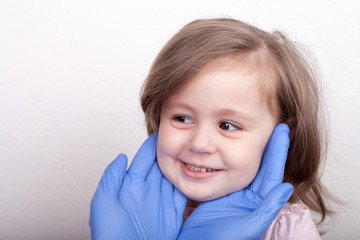 A doctor in blue gloves holds a cute girl behind her cheeks