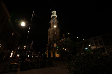 High bell tower of city hall in a characteristic medieval town with monumental medieval houses and atmospheric illuminated squares full of terraces. 