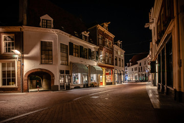 Fototapeta na wymiar Cozy winding shopping street with illuminated shops in a characteristic medieval town. Monumental medieval houses in Historic old fortified town in the Netherlands 