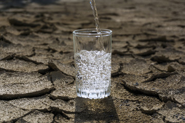 pure clear fresh water is poured into a glass beaker standing in the middle of a dry cracked clay...