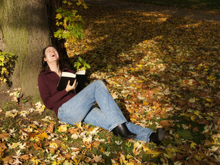 woman laughing out loud while reading a book in autumn scene
