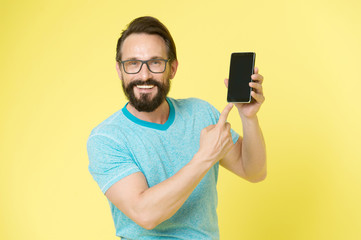 Man excited about new mobile opportunities. Guy eyeglasses cheerful pointing at smartphone. Man...